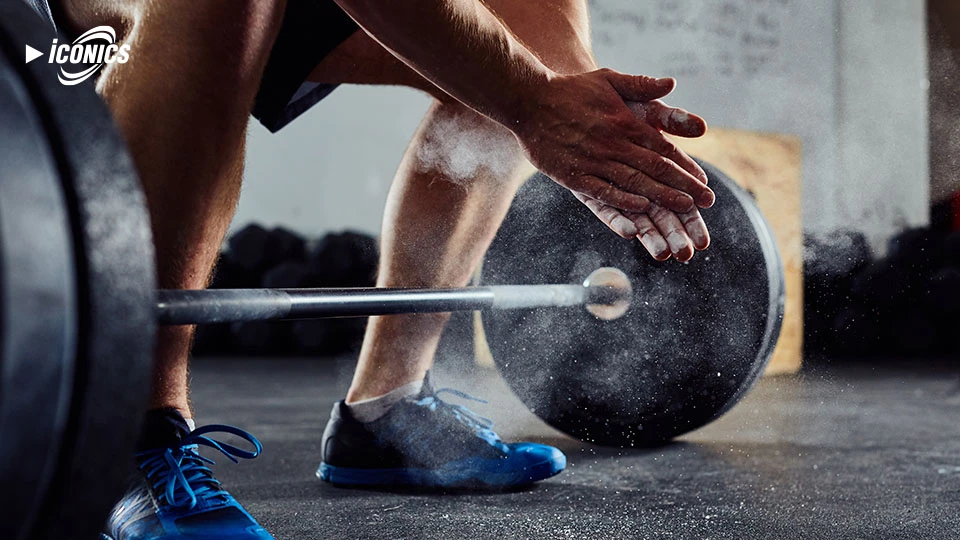 Picture  from inside a gym at floor level of hands chalking up at the weight bar for a deadlift