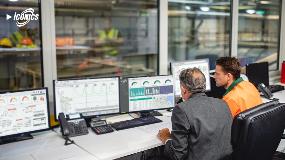 Photo of two men sitting at a desk with four monitors featuring various dashboard views